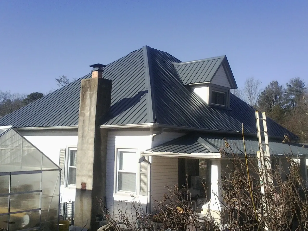 Dark blue standing seam metal roof on a white farmhouse with dormer — Slate & Tile Roof Repair by Roofing Brothers in San Martin