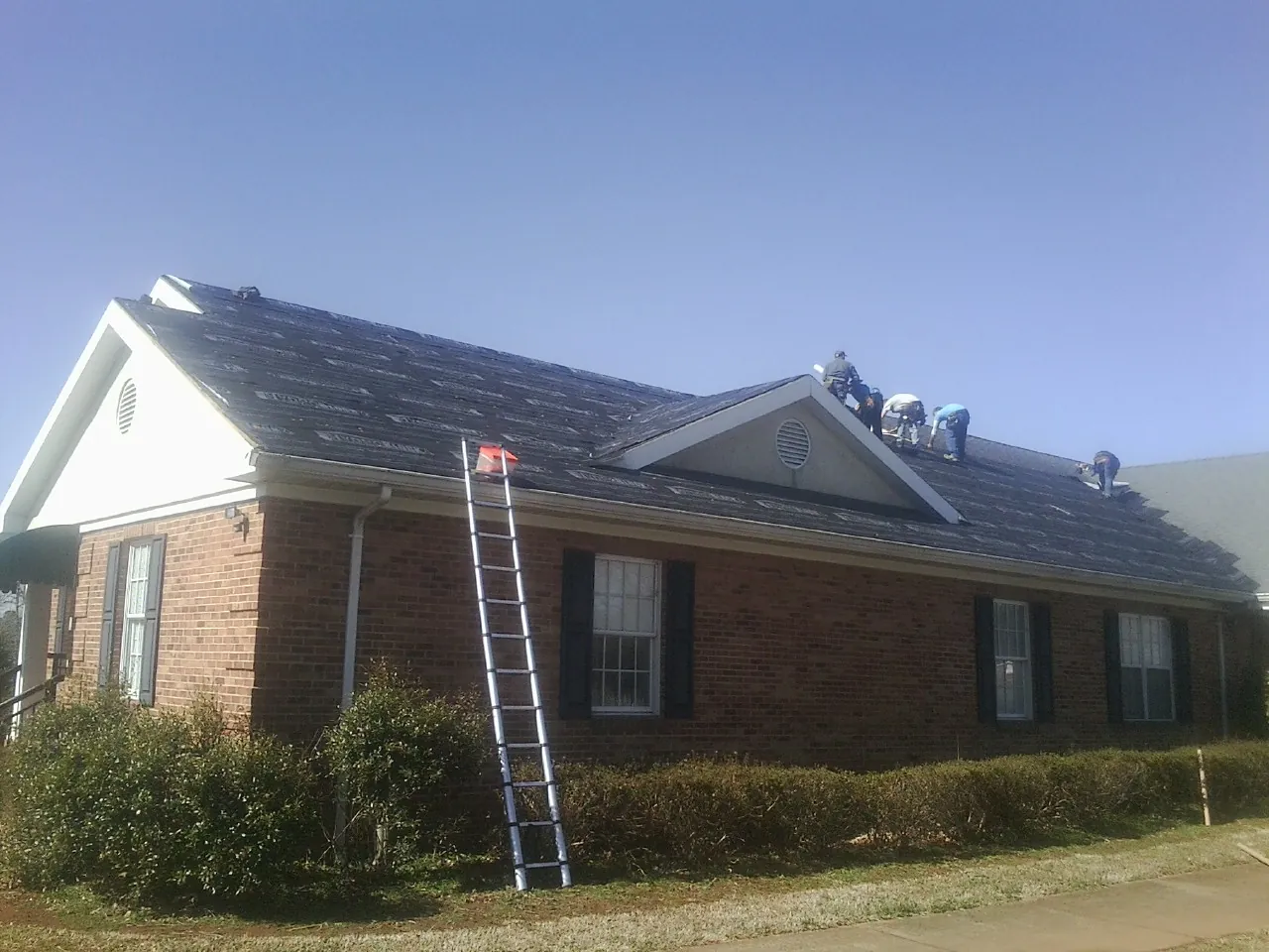 Crew tearing shingles off a brick ranch roof with a ladder set — Metal Roof Repair work by our crew in San Martin