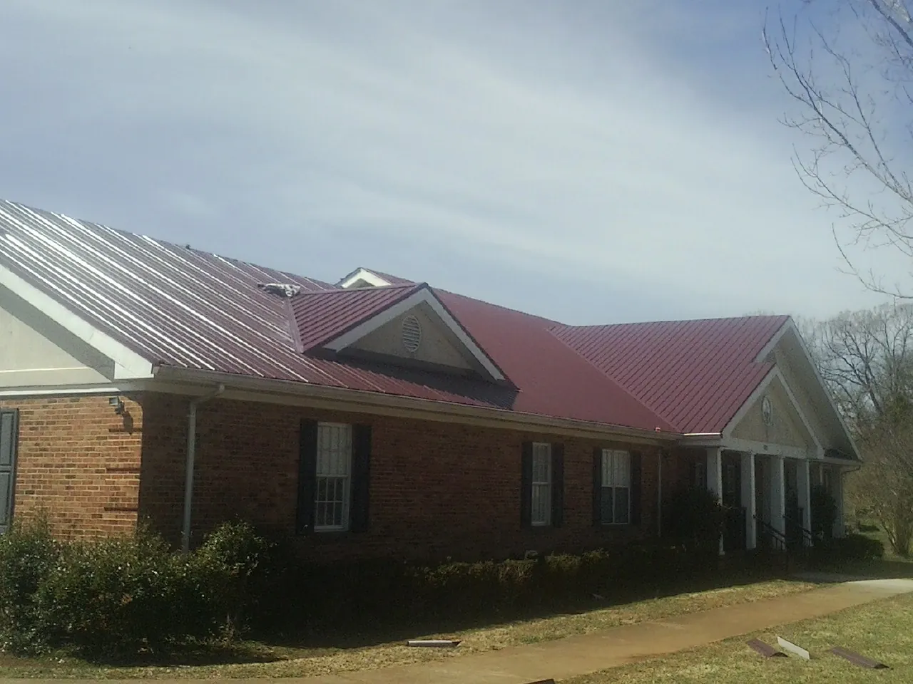 Red metal roof with gabled entries on a long brick building, from a Hail Damage Roof Repair job in San Martin