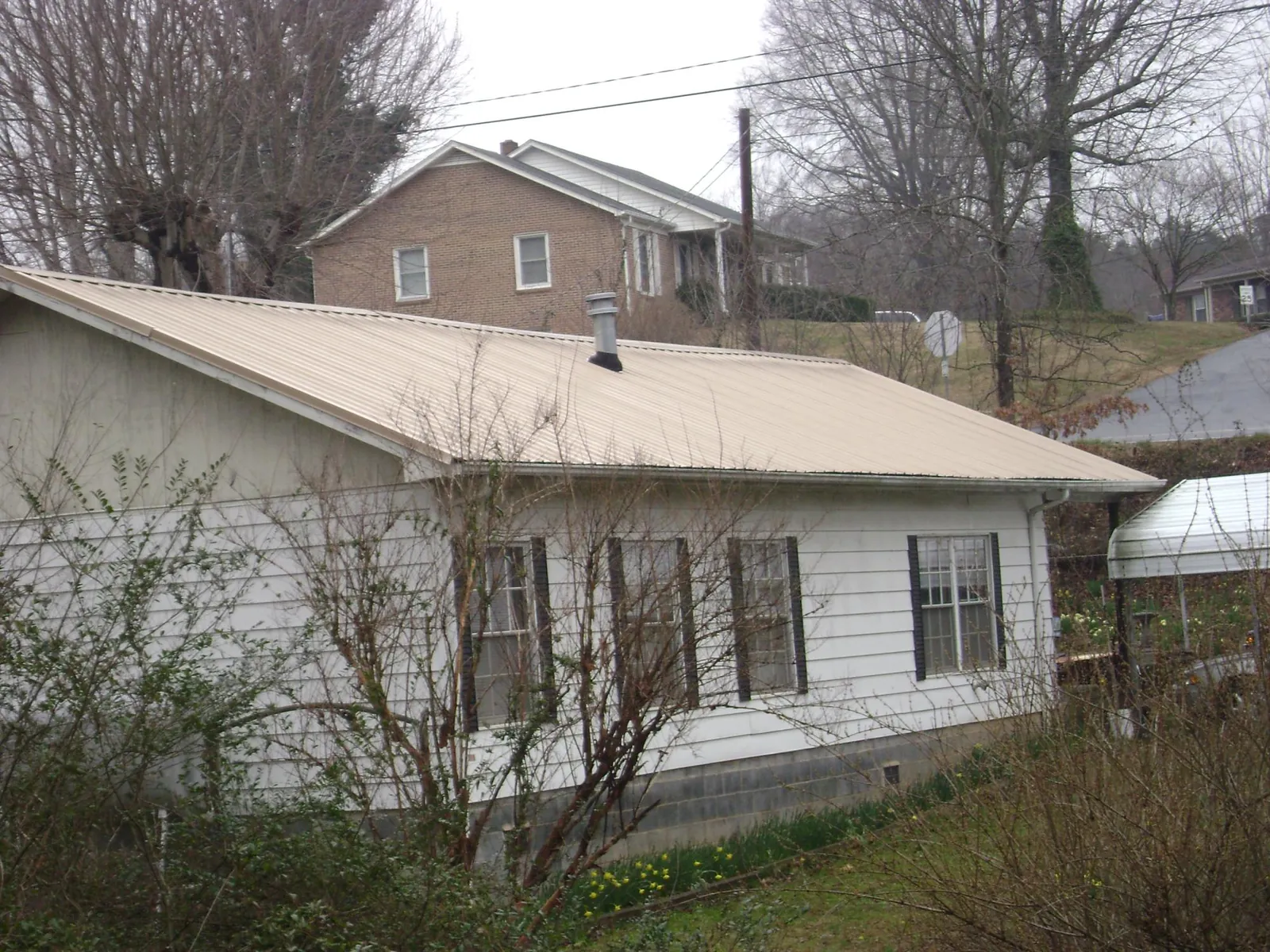 Tan metal roof on a white sided house set into a hillside — Commercial Roofing by Roofing Brothers in San Martin