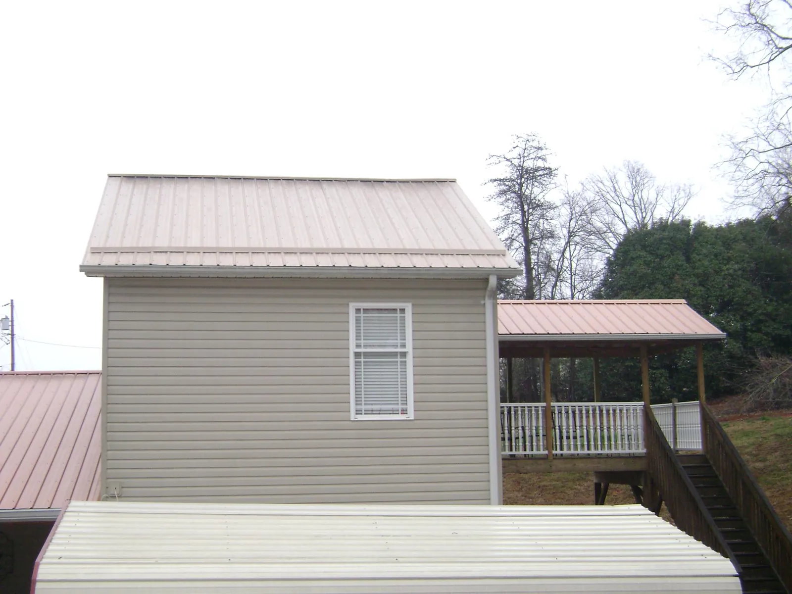 Tan metal roofs on a two story addition and attached porch, from a Roof Replacement job in San Martin